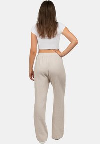 Beige, textuur brede broek met een elastische tailleband, van de achterkant getoond. Het materiaal heeft een wafelpatroon en biedt een ontspannen pasvorm.