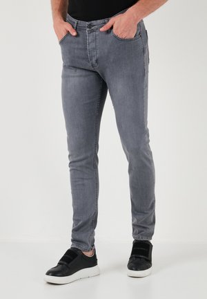 Szare jeansy slim fit wykonane z denimu, z pięcioma kieszeniami, delikatnym przecieraniem i zapięciem na guzik. Noszone z czarnymi trampkami na slip-on.