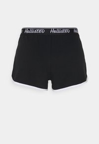 Černé šortky s bílým lemem na spodním okraji, s pasem označeným nápisem "Hollister" bílým písmem na černém pozadí.