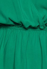Abito in tessuto verde con vita arricciata, texture liscia e design drappeggiato con fronte incrociato. Nessun hardware o motivo visibile.