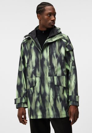 Chaqueta verde y negra con un estampado, cierre con cremallera, capucha ajustable y múltiples bolsillos. Textura suave y corte holgado.
