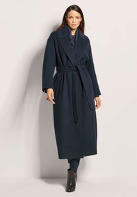 Marineblauwe wollen trenchcoat met een wikkeldesign, brede revers, riem in de taille, zijzakken en lange mouwen. Gladde textuur en klassieke snit.