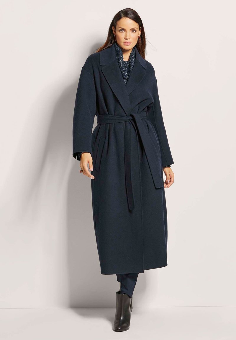 Marineblauwe wollen trenchcoat met een wikkeldesign, brede revers, riem in de taille, zijzakken en lange mouwen. Gladde textuur en klassieke snit.