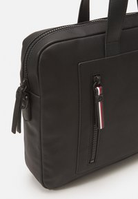 Borsa per laptop nera con texture, di forma rettangolare, dotata di cerniera superiore e una tasca frontale con un tirante a cerniera a righe rosso, bianco e blu.