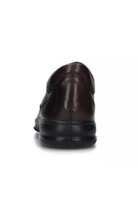 Sneaker in pelle marrone con tacco arrotondato, suola in gomma nera e dettagli di cucitura minimi, visto da dietro su uno sfondo bianco.