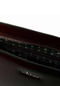 Bolso de mano de cuero color burdeos con cierre de cremallera, equipado con un forro interior negro con pequeños patrones de corazones blancos y herrajes plateados pulidos.