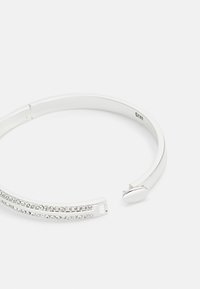 Sølv mansjettarmbånd med to parallelle rader av klare rhinesten langs fronten. Jevn, polert overflate med et subtilt låsdesign.