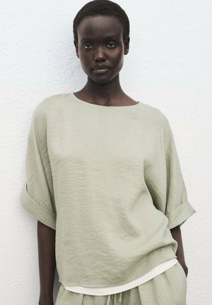 Light green linen top with a relaxed fit, wide sleeves, and a round neckline. Features a textured finish and a cream accent at the hem.