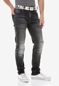 Schwarze Jeans aus Denim mit einem verblassten Finish, mit Steppnähten, geradem Schnitt und einem weißen Gürtel mit roten Akzenten.