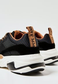 Černé sportovní tenisky vyrobené z kombinace texturované síťoviny a semiše, se béžovým akcentem a logem na patě. Kontrastní bílá podrážka.