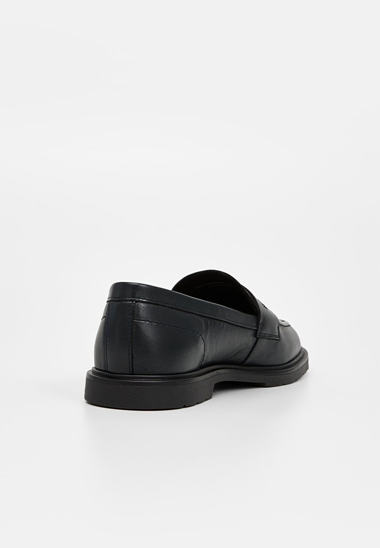 Chaussure noire en cuir à enfiler avec un profil bas, un bout arrondi et un design minimaliste. Fini mat et semelle en caoutchouc robuste avec une légère texture.