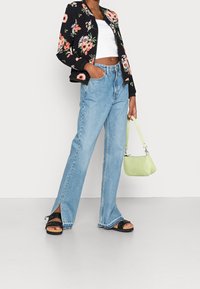 Czarna bomberka w kwiaty, biały krótki top, jasnoniebieskie jeansy z wysokim stanem i bocznymi rozcięciami, czarne sandały, zielona torebka o fakturowanej powierzchni.