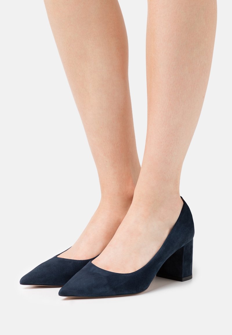 Escarpins à talons hauts en daim bleu marine avec un bout pointu et un talon bloc. Présentent une texture lisse et un design minimaliste.