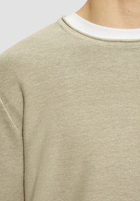 Lichtbeige trui met een textuur gebreide afwerking, met een ronde hals en een witte binnenkraag. Eenvoudig, modern ontwerp.