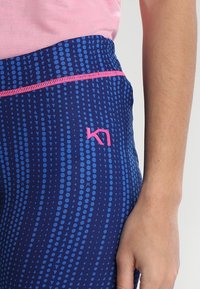 Marinblå leggings med en strukturerad mönster av blå cirklar och trianglar. Har en rosa midjeband och logotypdetalj. Slätt, elastiskt material.