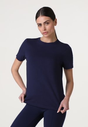 T-shirt blu navy a maniche corte realizzato in tessuto liscio, con collo rotondo e design aderente, indossato sopra leggings sportivi coordinati.
