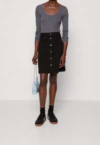 Musta farkkuhame, jossa edessä napitus, yhdistetty harmaaseen pitkähihapaiseen yläosaan ja mustiin lenkkareihin. Pitelee vaaleansinistä käsilaukkua.