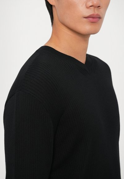 Sweater preto com textura canelada apresentando um design de decote em V, exibindo textura vertical e uma silhueta ajustada, disponível numa cor sólida.