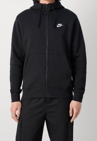 Musta vetoketjullinen huppari, joka on valmistettu puuvillasekoitteesta. Siinä on etutasku, säädettävä nyörihuppu sekä valkoinen Nike-logo vasemmassa rinnassa.