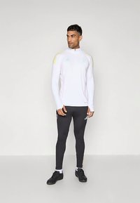 Bluză sportivă albă cu mâneci lungi, cu accente roz și galbene, asortată cu pantaloni negri mulați. Prezintă logo-urile Adidas pe ambele piese și un guler înalt.