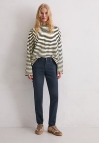 Gestreepte blouse met lange mouwen in crème en zwart, marineblauwe broek en bruine sneakers met gemengde texturen. Minimalistisch ontwerp, relaxte pasvorm.