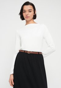 Λευκό τοπ με μακριά μανίκια συνδυασμένο με μαύρη φούστα, τονισμένο με καφέ ζώνη. Ομαλή υφή με απλή, μοντέρνα σιλουέτα.