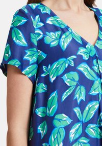 Top azul de manga corta con escote en forma de V y un gran estampado de hojas verdes con detalles en blanco, hecho de una tela suave y ligera.