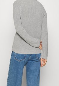 Pull en maille gris avec texture côtelée et manches longues, associé à un jean en denim bleu clair avec un design classique à cinq poches.