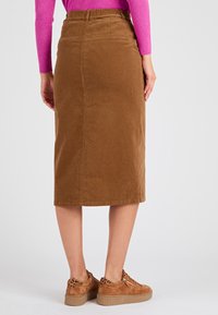 Falda midi de pana marrón con silueta recta, bolsillos traseros y cintura alta, combinada con zapatillas beige que tienen detalles de estampado de leopardo.