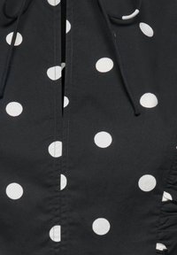 Tissu noir à gros pois blancs, avec une couture centrale et des cordons en haut.