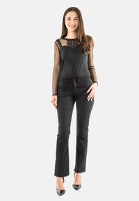 Top negro de manga larga con mangas transparentes con puntos y cuerpo sólido, combinado con pantalones ajustados negros y tacones brillantes negros.