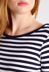 Haut à rayures bleu marine et blanc à manches longues avec un large col bateau, présentant un matériau en coton doux et une silhouette ajustée.