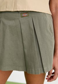 Gonna plissettata verde oliva realizzata in tessuto misto cotone, con orlo cucito e un piccolo patch del logo Dickies sulla vita.