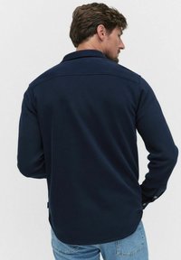 Mörkblå långärmad skjorta med en texturerad yta, med krage, knappdetalj på ärmarna och en rundad nederkant. Lämplig för vardagsbruk.