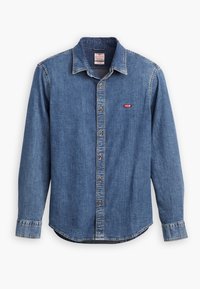 Camicia di jeans a maniche lunghe di blu medio con colletto button-down, caratterizzata da un logo rosso Levi's e bottoni marroni. Texture sbiadita lungo le cuciture.