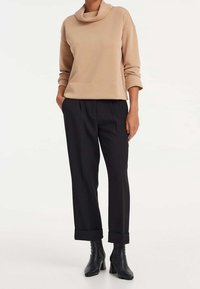 Maglione beige a collo a risvolto con maniche lunghe, abbinato a pantaloni neri dal taglio morbido con risvolti. Stivaletti neri con tacco.