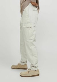 Pantaloni cargo beige realizzati in cotone, dotati di tasche laterali, vestibilità rilassata e una texture liscia. Abbinati a scarpe in suede marrone chiaro.
