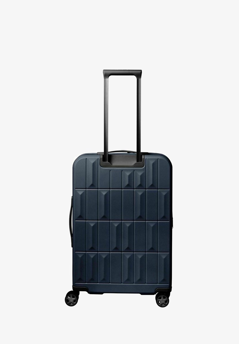 Valise rigide bleu marine à motif géométrique, poignée télescopique noire étendue, quatre roues et poignée de transport latérale.