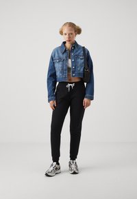 Cropped denim jacket, grey crop top, black sweatpants with drawstring, and sporty shoes with white, black, and silver accents.
