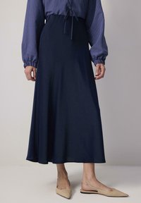 Jupe longueur au sol bleu marine en tissu fluide, avec une ceinture élastique. Associée à des chaussures slingback beige à bout pointu.