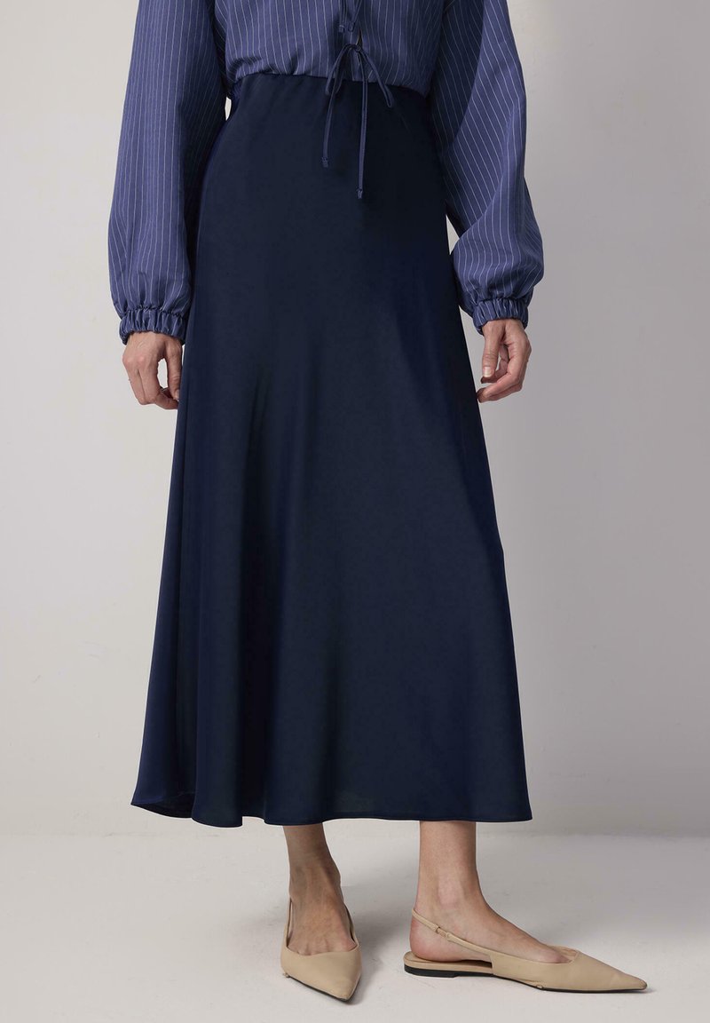 Jupe longueur au sol bleu marine en tissu fluide, avec une ceinture élastique. Associée à des chaussures slingback beige à bout pointu.