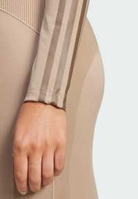 Top sportivo beige con maniche lunghe caratterizzato da strisce marroni lucide lungo le braccia. Tessuto liscio e aderente con una texture a costine sul collo.