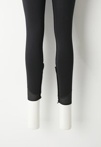 Leggings de sport noirs avec une coupe ajustée, présentant des accents en maille au niveau des poignets et des zips sur les côtés pour plus de détail et de ventilation.