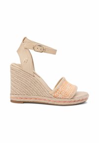 Sandale compensée beige avec talon tressé, bride cheville avec boucle, et bride avant avec détail tissé en pêche et beige.