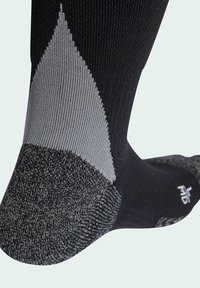 Čierna a sivá športová ponožka s rebrovanou textúrou, vystuženou pätou a geometrickým dizajnom na manžete. Obsahuje logo na podrážke.