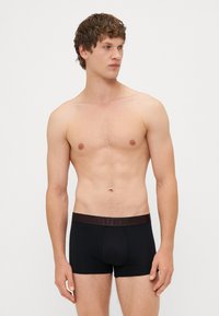 Boxer slip neri con un elastico marrone in vita, su cui è stampato il logo "GUESS". Tessuto morbido e design aderente.