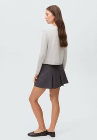 Top lung cu mâneci lungi de culoare gri deschis, cu decolteu rotund, asortat cu o fustă plisată neagră. Modelul poartă pantofi plate negri cu ținte.