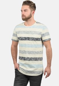 Tricou cu dungi realizat din bumbac, având dungi orizontale de culoare albastru deschis, bej și albastru închis, cu guler rotund și mâneci scurte.