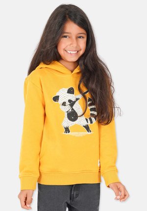 Gelbes Kapuzenoberteil mit einem Panda-Graphic. Weiches Material, gerippte Bündchen und Saum. Über einer dunkelgrauen Hose getragen.