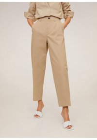 Pantalons en coton beige à coupe ajustée, dotés de poches avant et d'une fermeture à un bouton, associés à des sandales blanches tressées.